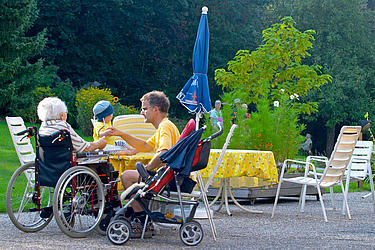 Alte Dame im Rollstuhl, Vater mit Kleinkind auf der Terrasse