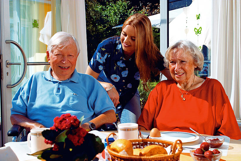 Älteres Paar mit Pflegerin am Frühstückstisch