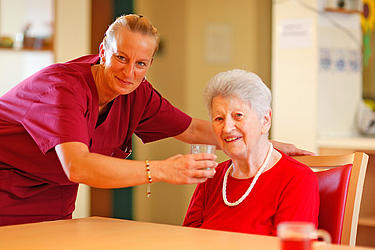 Pflegerin und Bewohnerin lachend mit Glas